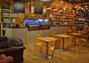 A cafe area with wooden floors and both padded armchairs and upright seating.