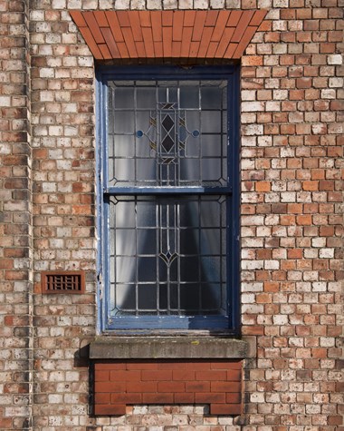 Sash window with stained glass set in brick building.