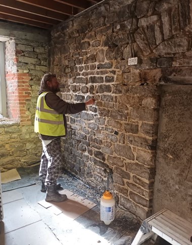 A stonemason repairs the interior of a historic building with exposed stonework.